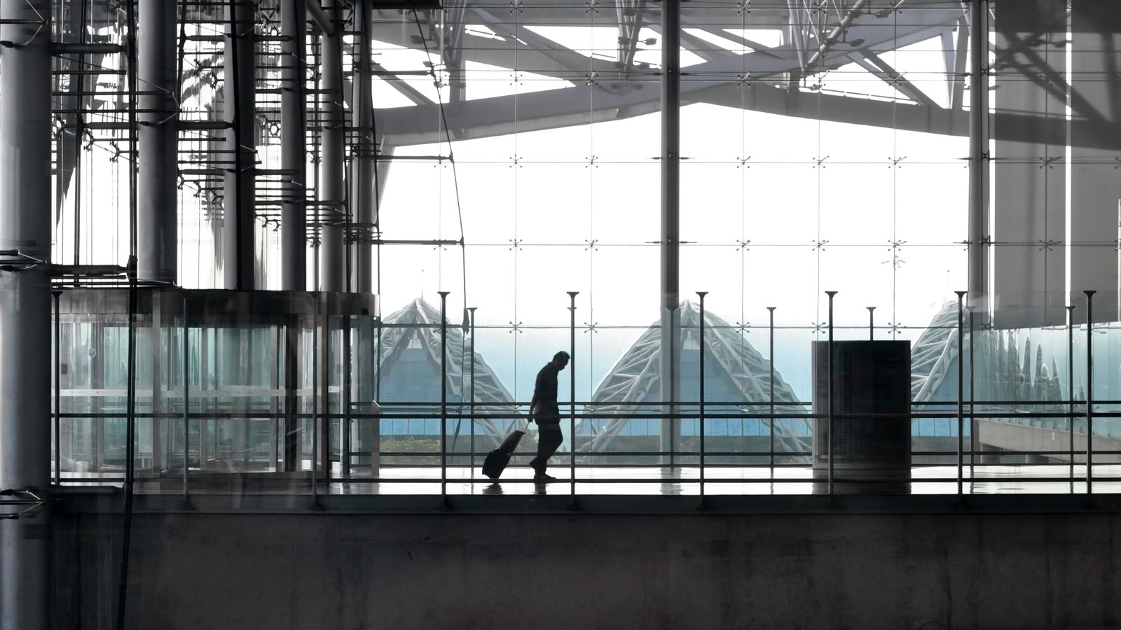 スーツケースを引いて空港ターミナルの通路を歩く旅行者(イメージ)