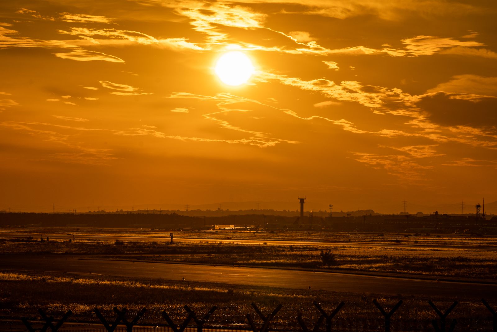夕日に染まる空港の滑走路と遠くに立つ管制塔のシルエット(イメージ)