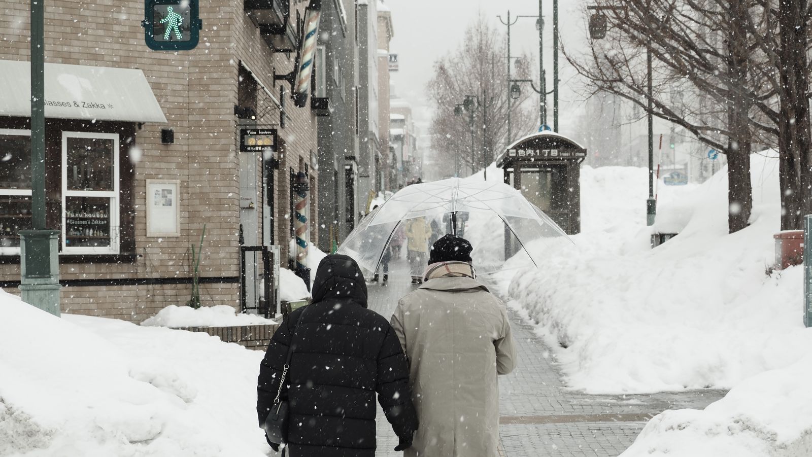 雪が積もった札幌の歩道を傘をさして歩く人々
