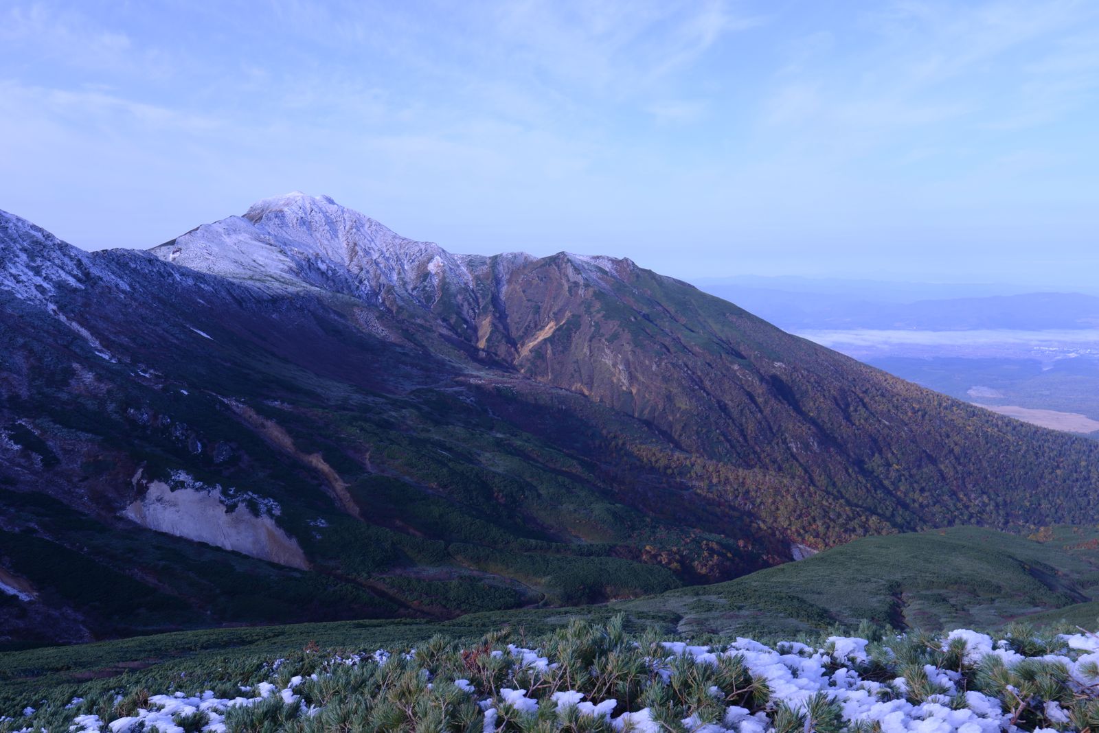 初雪をまとった北海道の山並みと紅葉の残る斜面
