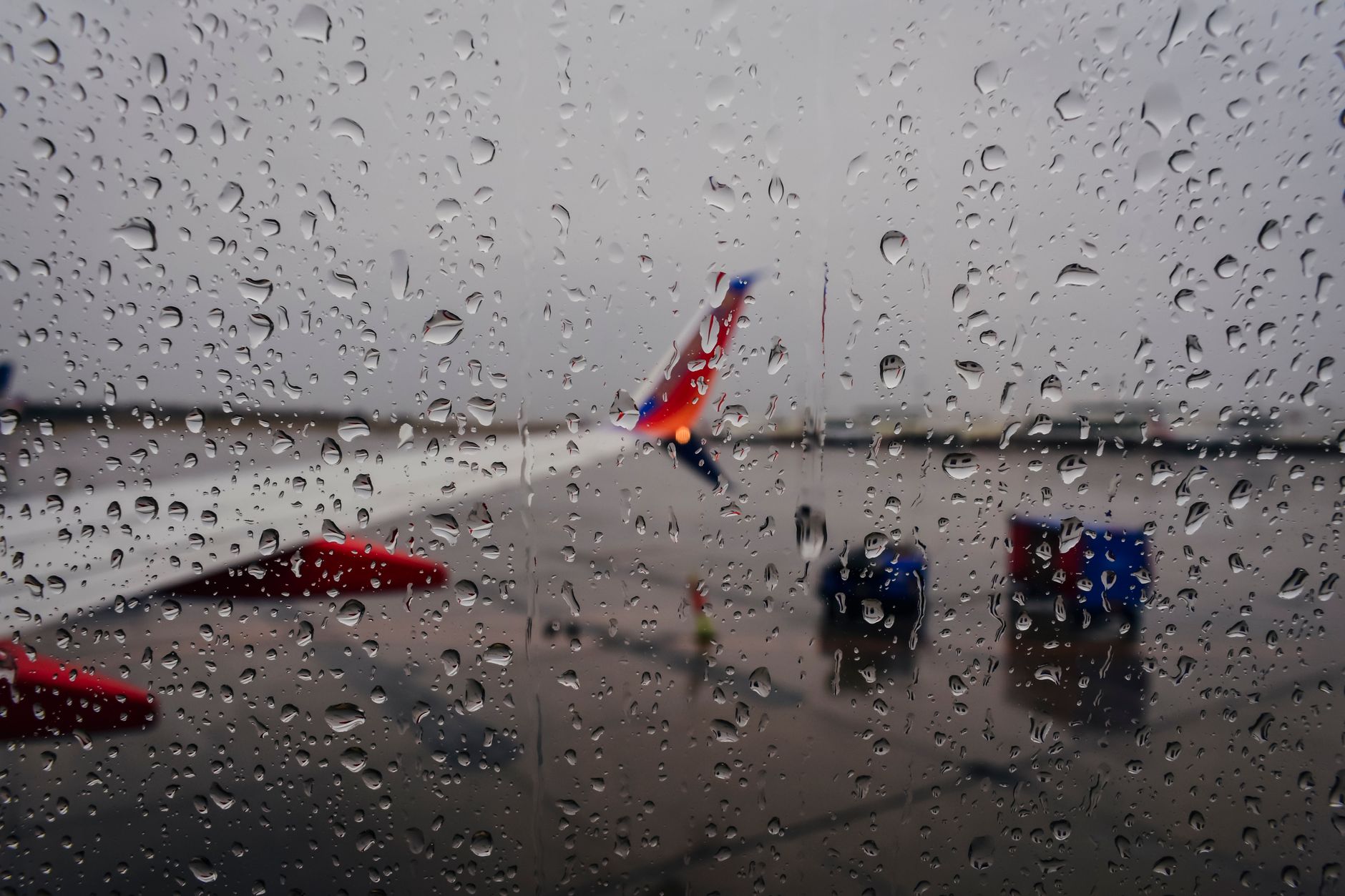 雨粒がついた窓の向こうに見える駐機中の旅客機(イメージ)
