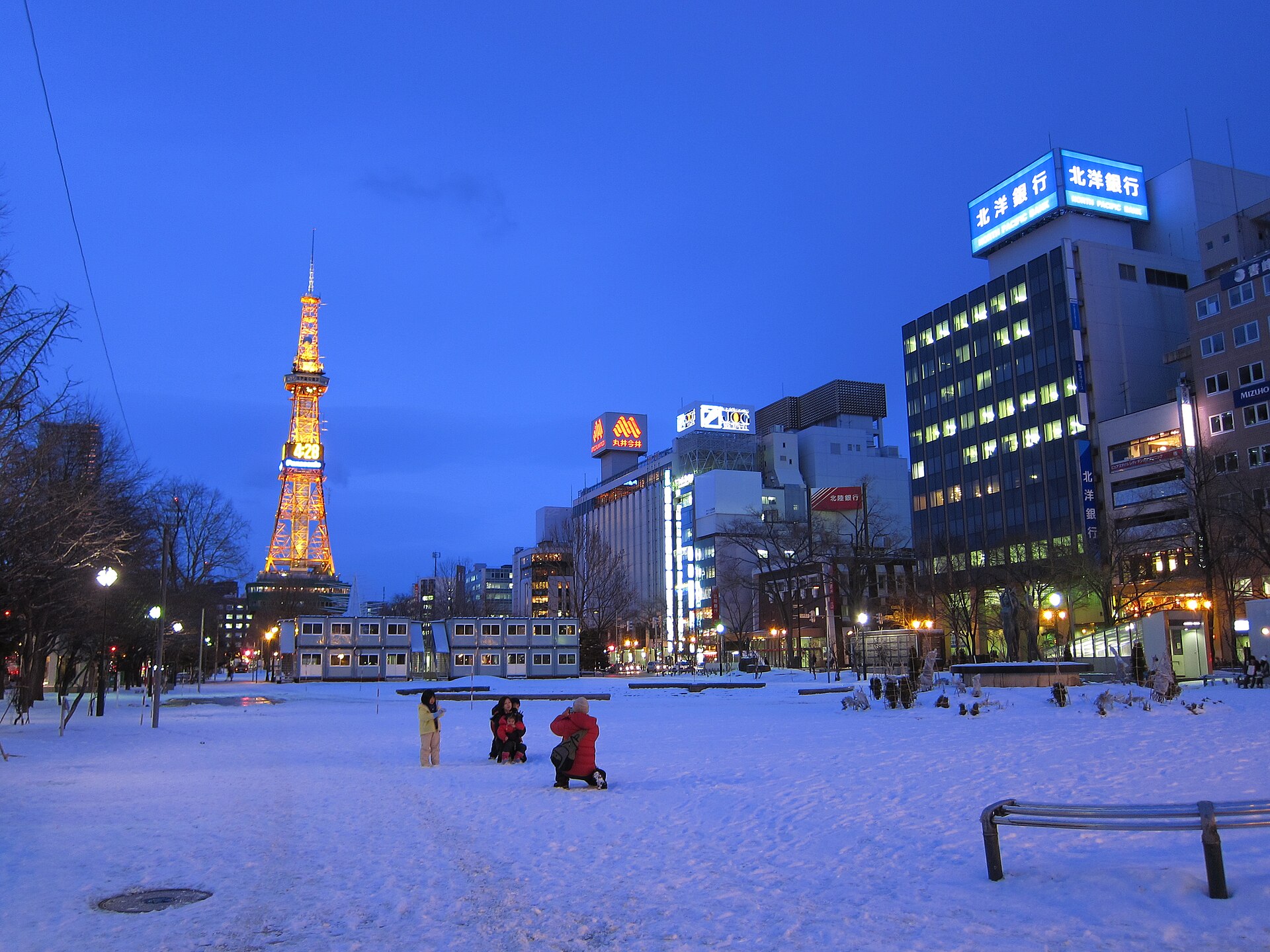夕暮れの大通公園。雪の積もった園内の先にライトアップされたさっぽろテレビ塔が立つ