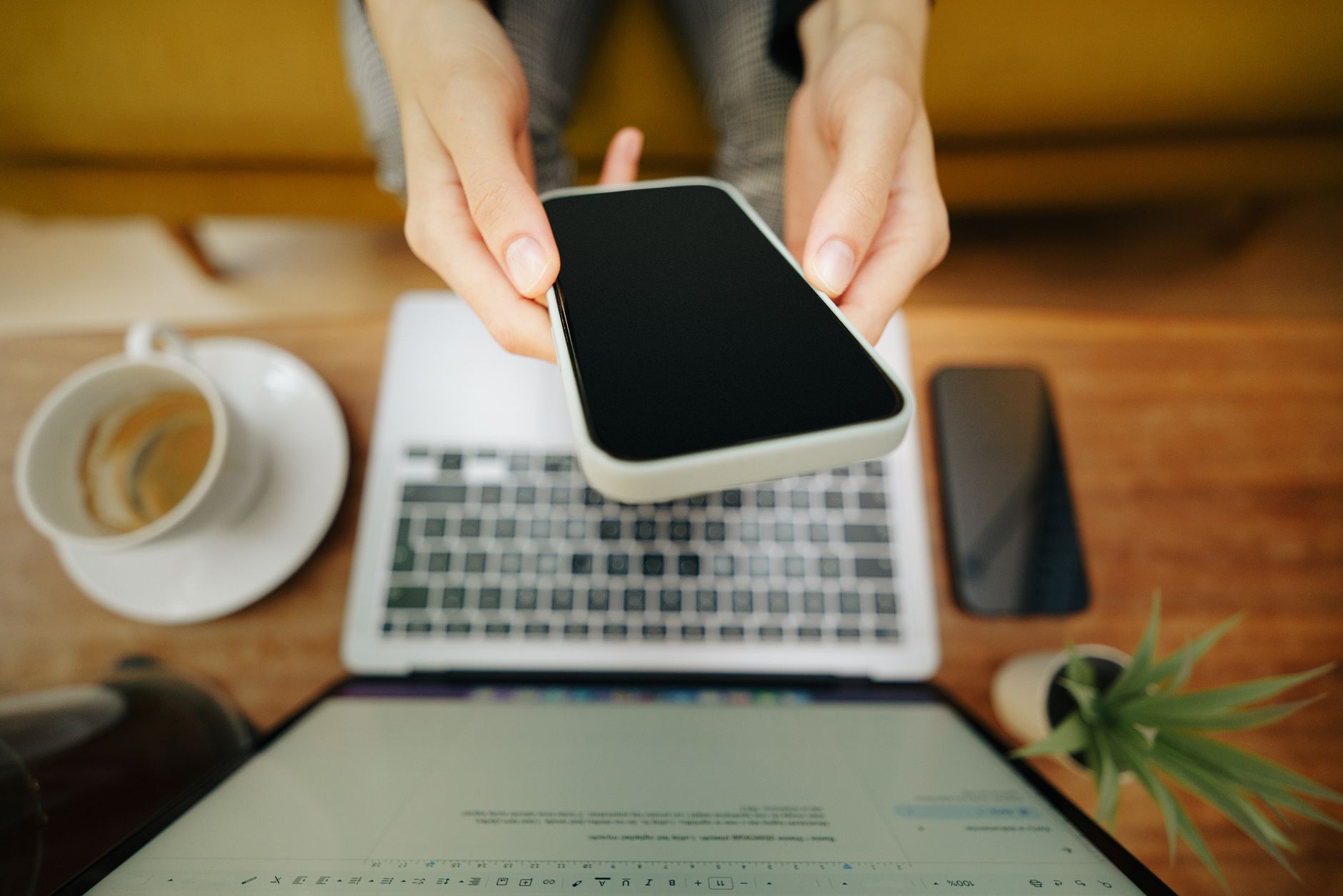 ノートパソコンの前でスマートフォンを手に取り予約操作をするところ(イメージ)