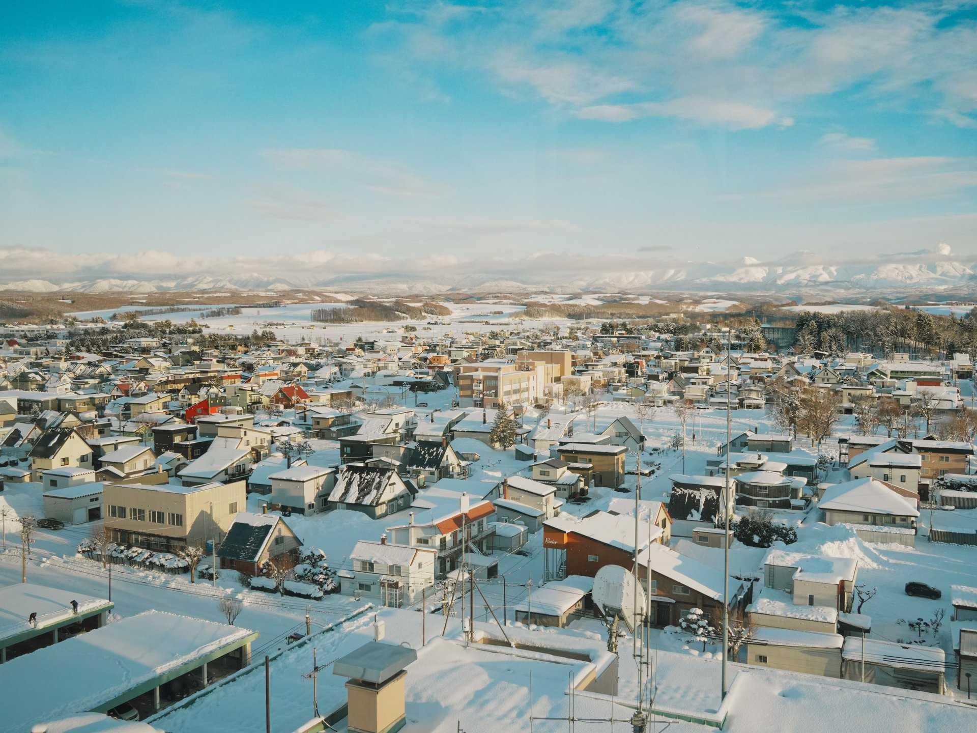 屋根や道路が雪に覆われた町並みを上空から見た風景