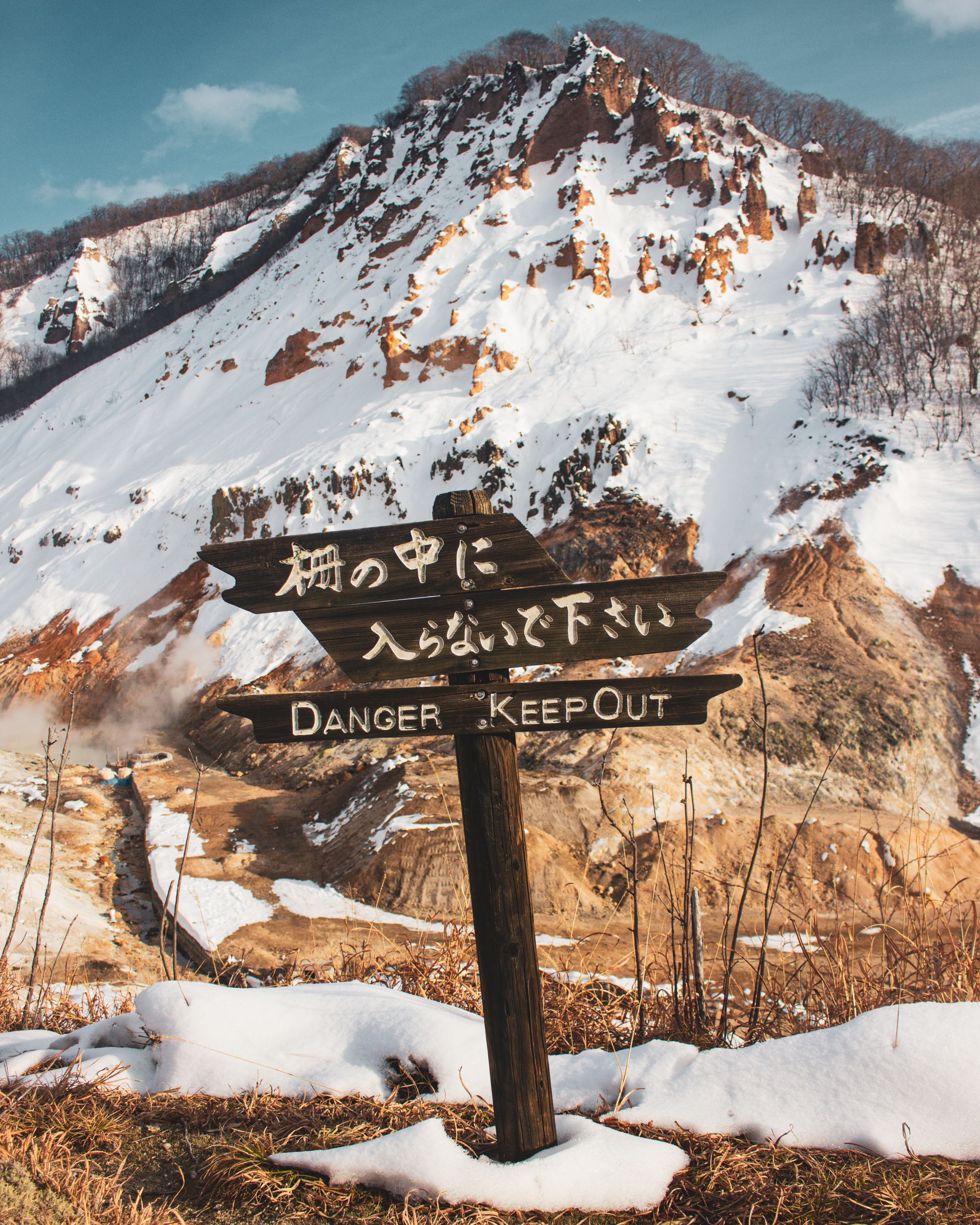 雪の登別地獄谷に立つ「柵の中に入らないで下さい DANGER KEEP OUT」の木製標識