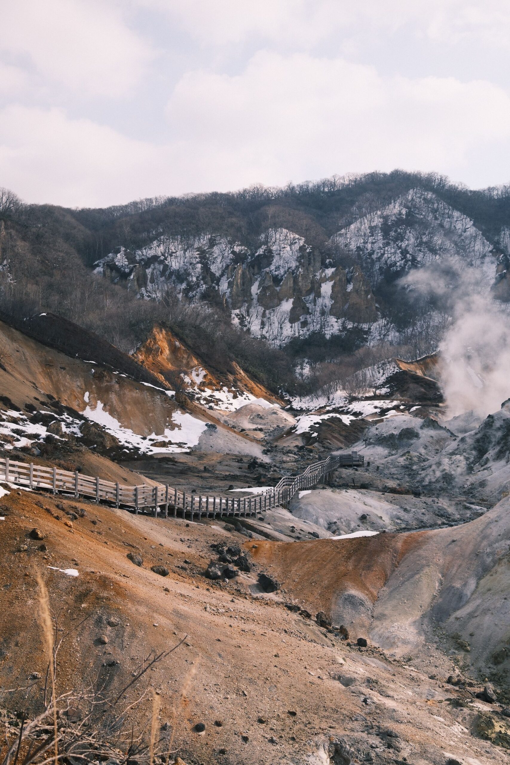 雪の残る斜面の間を延びる登別地獄谷の木道と立ち上る湯気