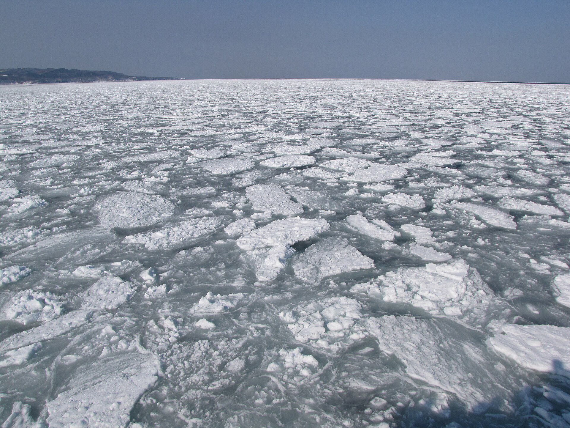 網走市の沖合いで見渡すかぎり海面を覆う流氷。遠くに雪をかぶった網走の海岸線が見える