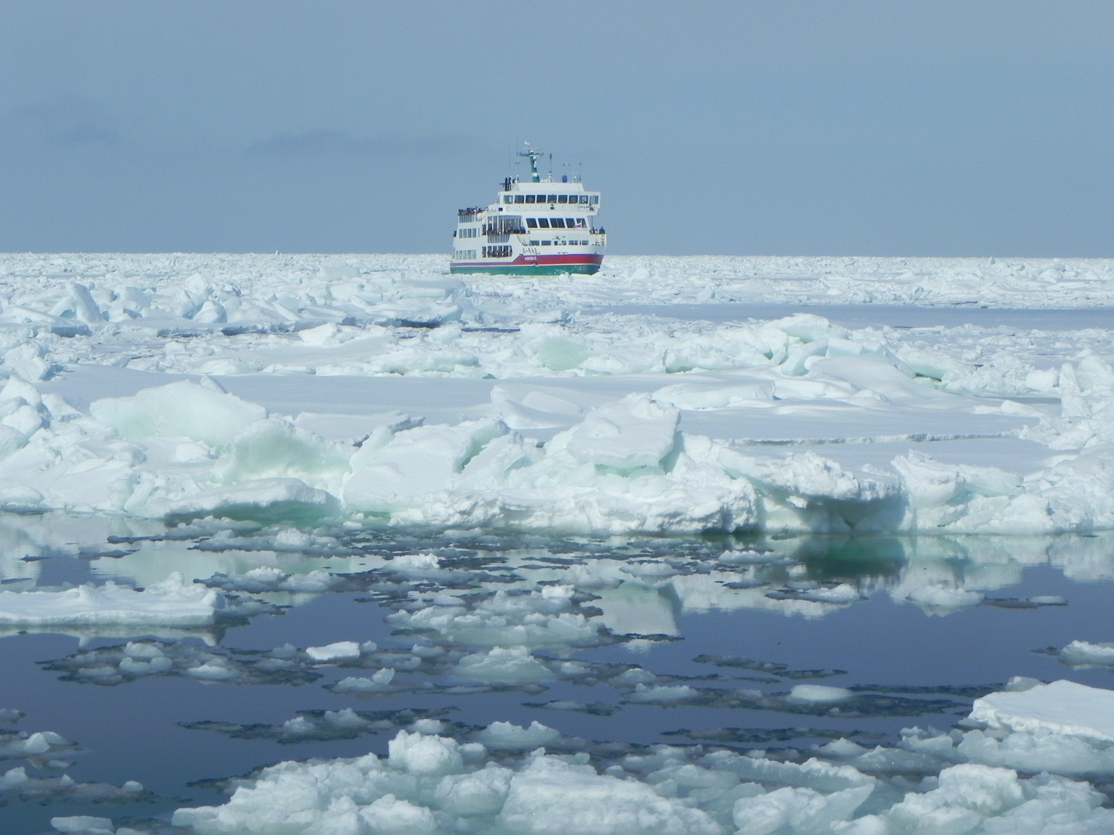 網走沖の流氷原を進む流氷観光砕氷船おーろら。船体の周囲は割れた氷で埋まり、手前に氷と黒い海面が広がる