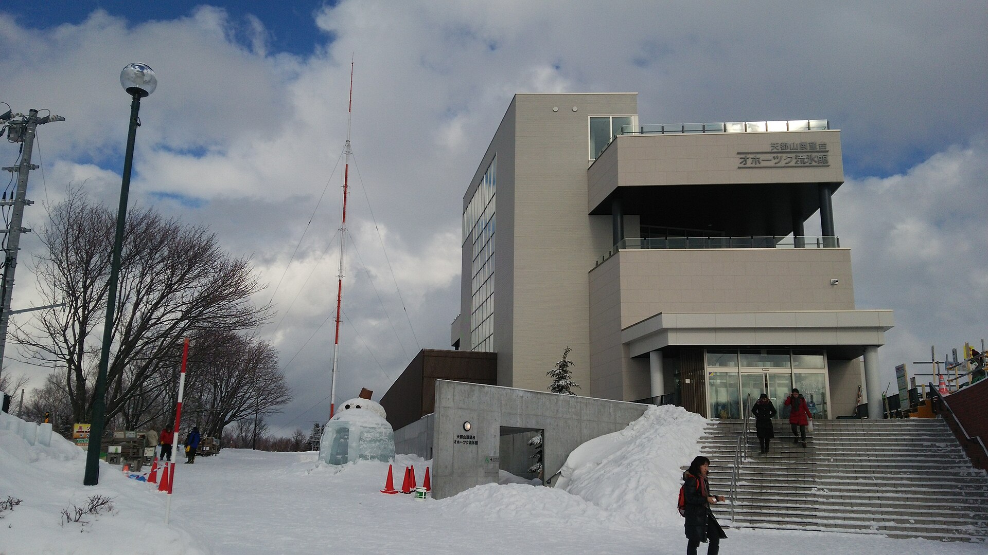雪に覆われた網走・天都山に建つオホーツク流氷館の外観。入口前の階段を訪問者が上っている