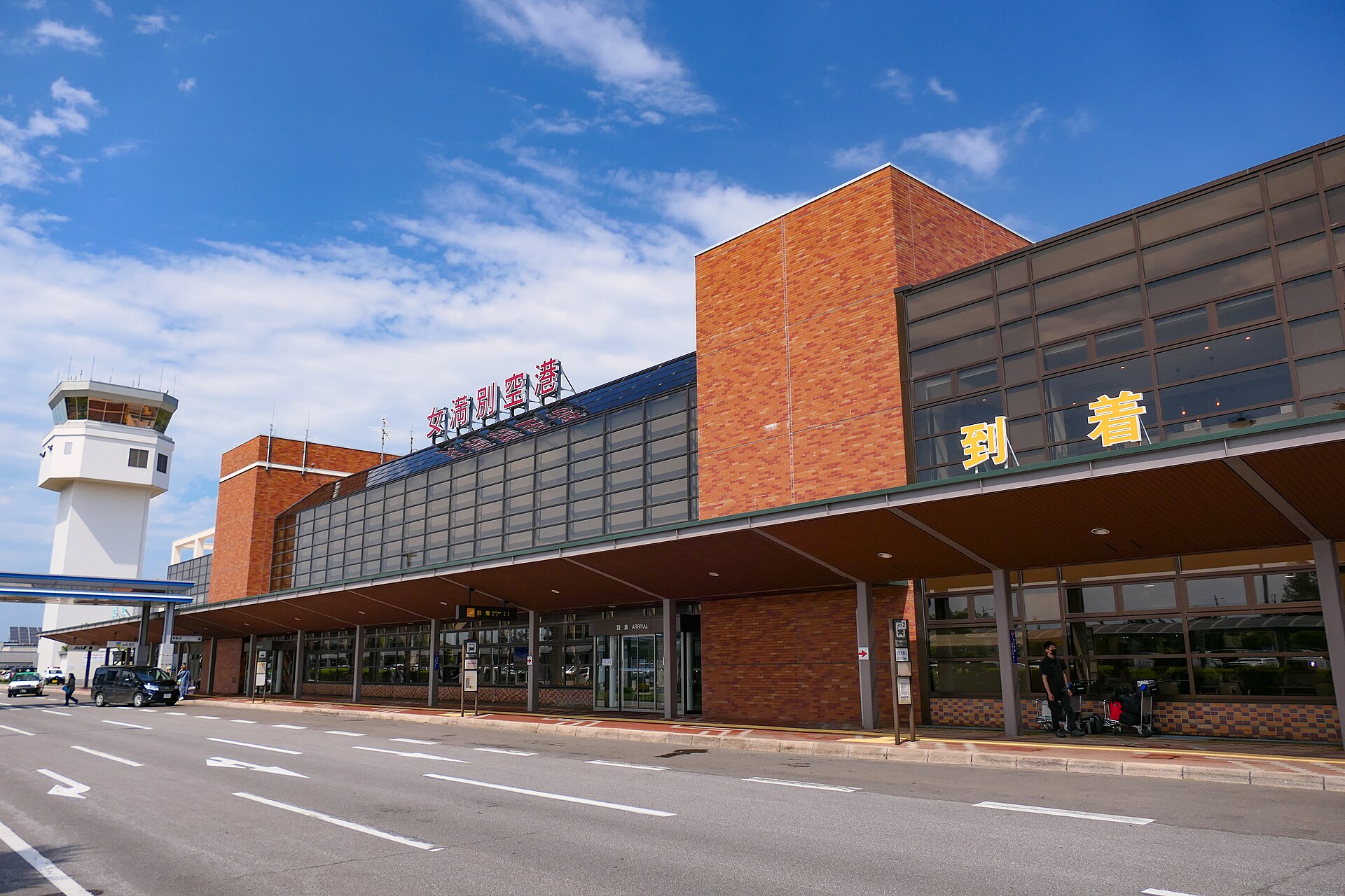 女満別空港ターミナルビルの外観。レンガ色の壁に「女満別空港」の看板と黄色い「到着」の文字、左手に管制塔が見える