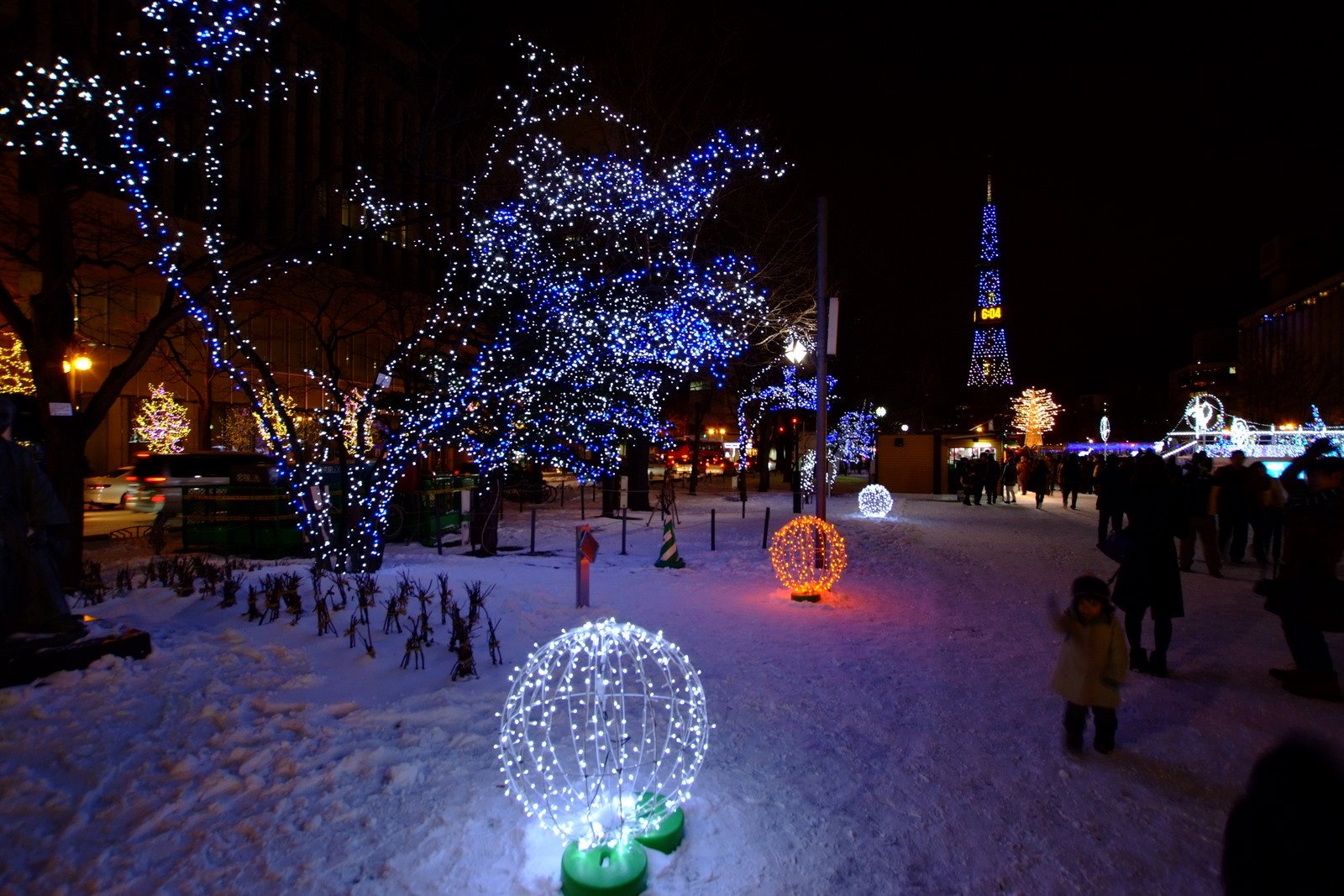 雪が積もった夜の大通公園。青白く光る木々と光の球のオブジェの奥に、さっぽろテレビ塔が見える