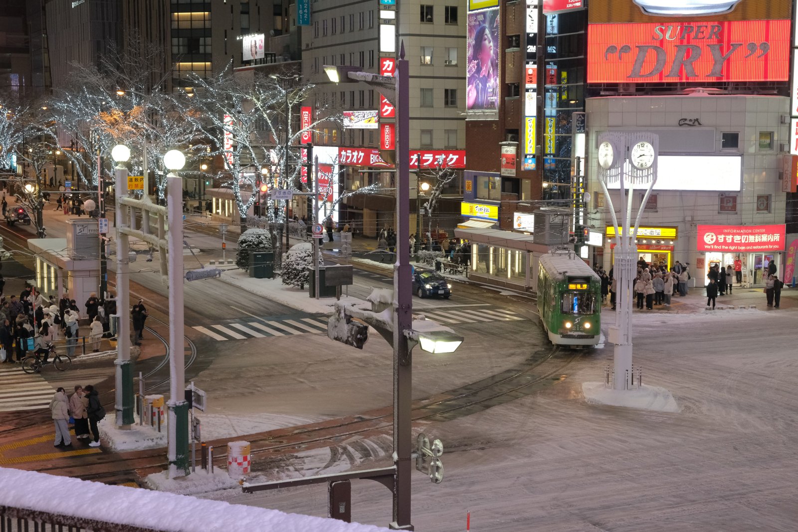 雪の積もったすすきのの交差点を走る路面電車と、白い電飾をまとった並木