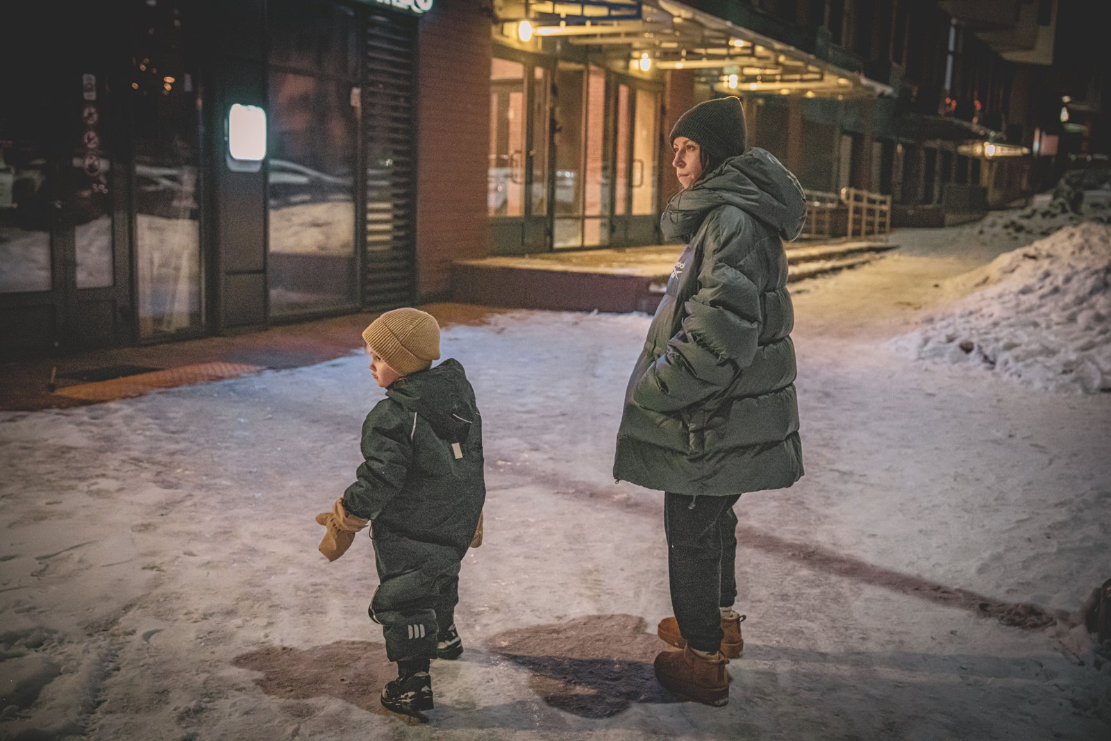 厚手のダウンジャケットと帽子で雪の夜道に立つ親子