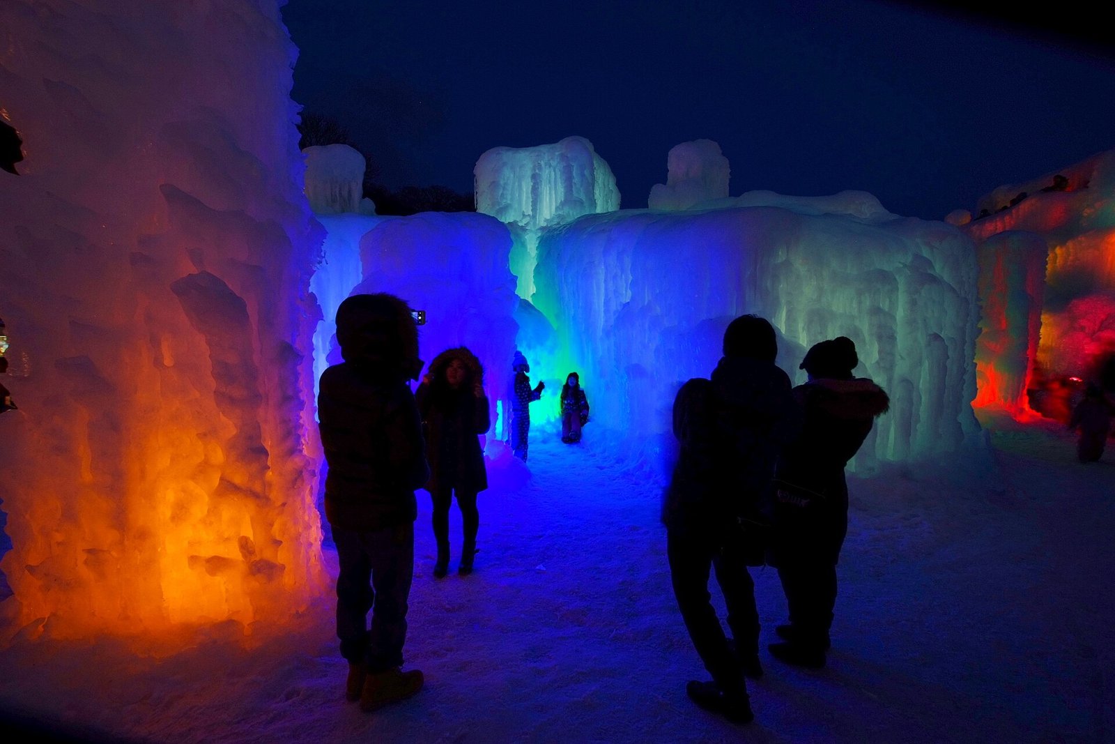 夜の支笏湖氷濤まつりで、青とオレンジに照らされた氷の間を歩く来場者のシルエット
