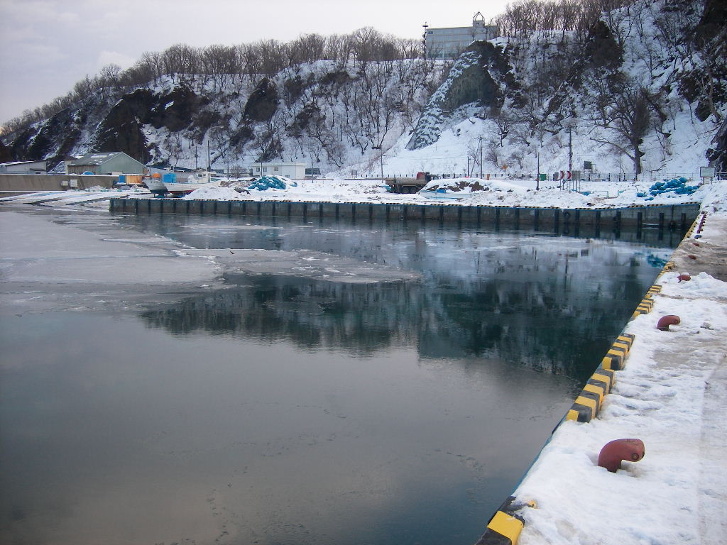 雪に覆われた冬のウトロの漁港。岸壁に雪が積もり、海面には薄い氷が浮かんでいる