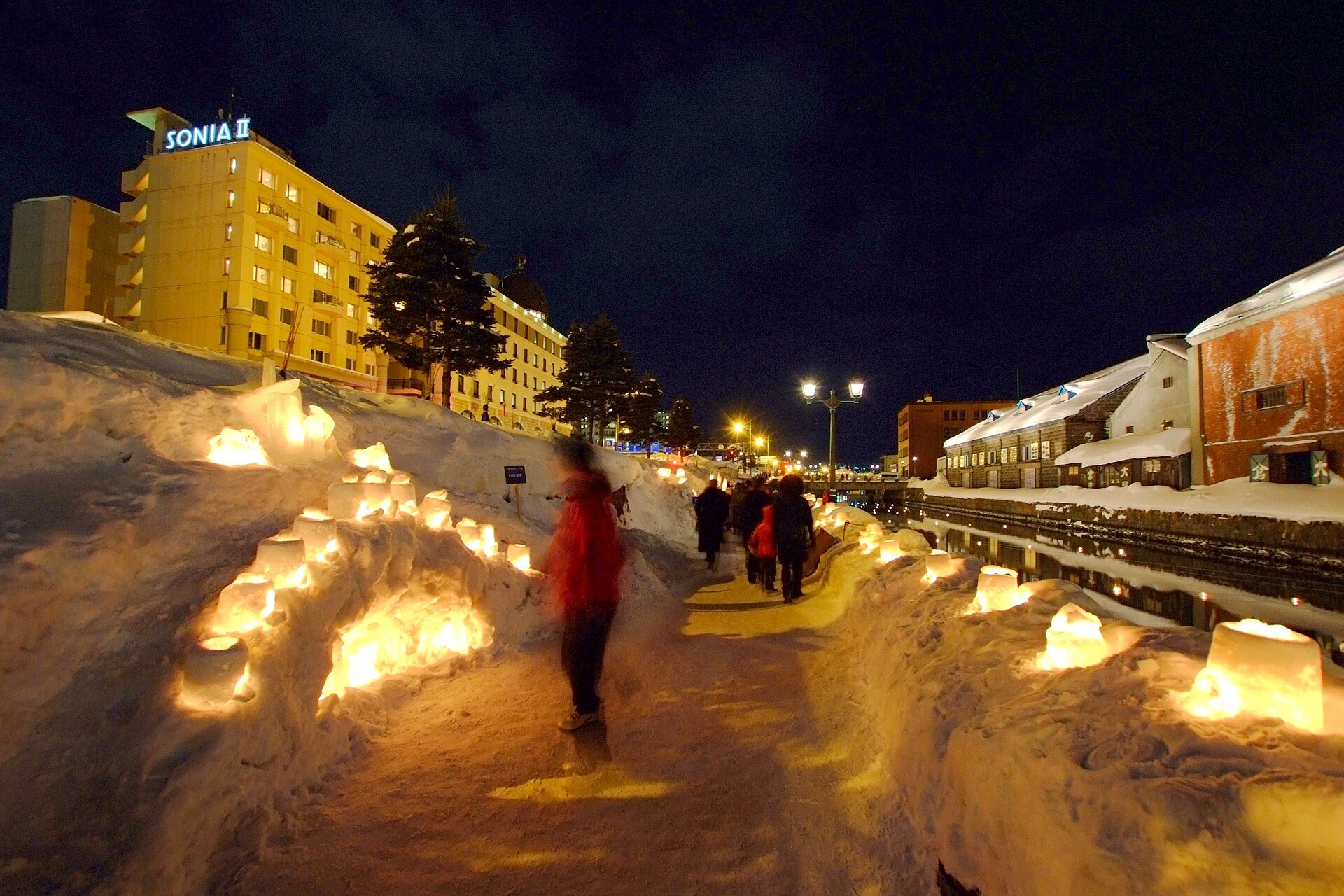 雪あかりの路の運河会場。雪の壁に埋め込まれたスノーキャンドルが続く運河沿いの遊歩道を歩く人々