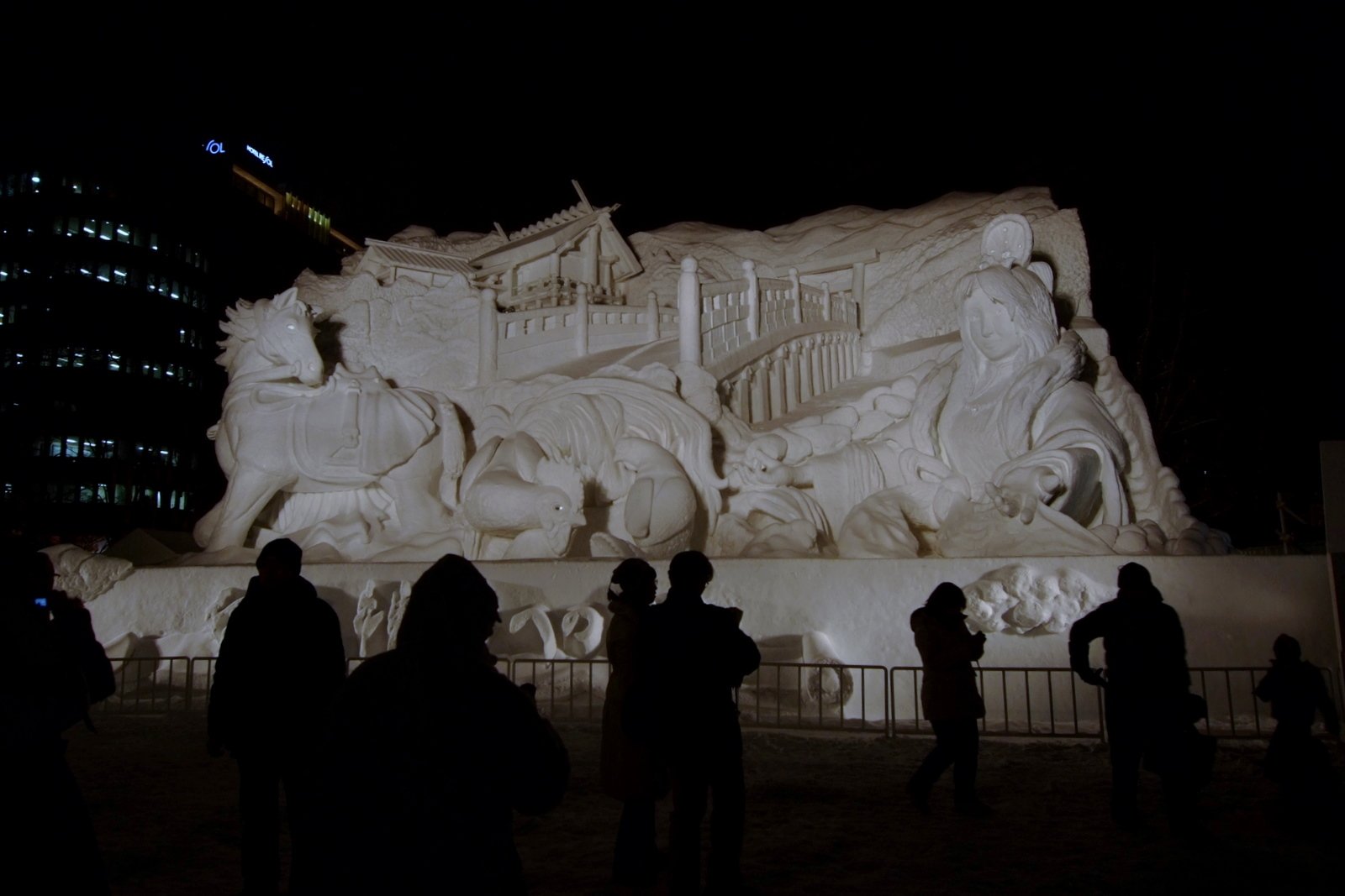 夜のさっぽろ雪まつり大通会場で、ライトアップされた大雪像の前に集まる見物客(第64回)