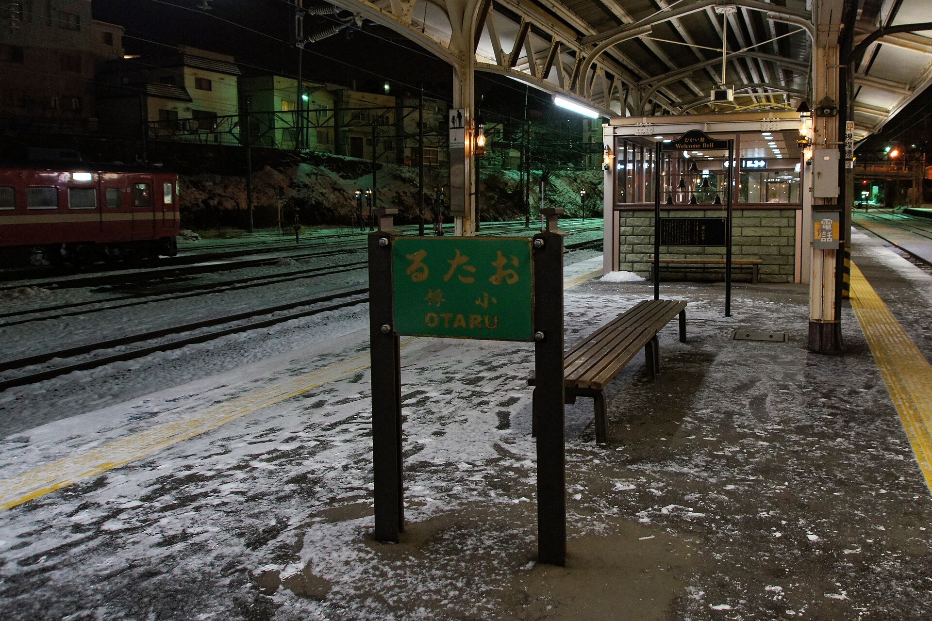 雪の積もった夜の小樽駅ホーム。「おたる」の駅名標とレトロな屋根