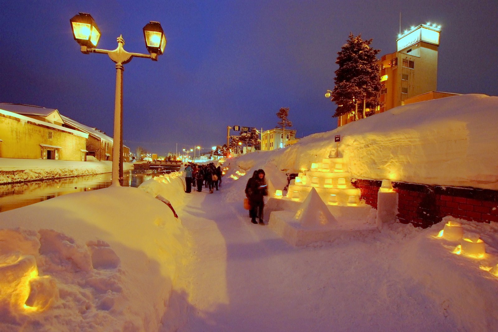 夕暮れの小樽運河沿い。ガス灯と雪の中に並ぶスノーキャンドル、灯りを見に訪れた人々