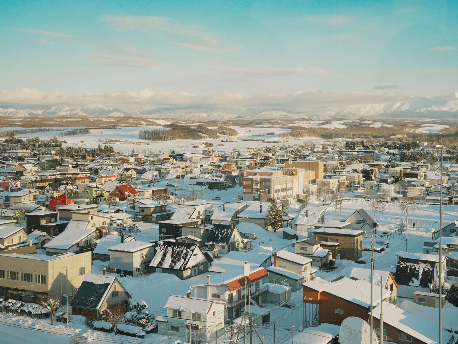 雪に覆われた家並みの向こうに雪山が連なる、北海道の冬の朝の風景