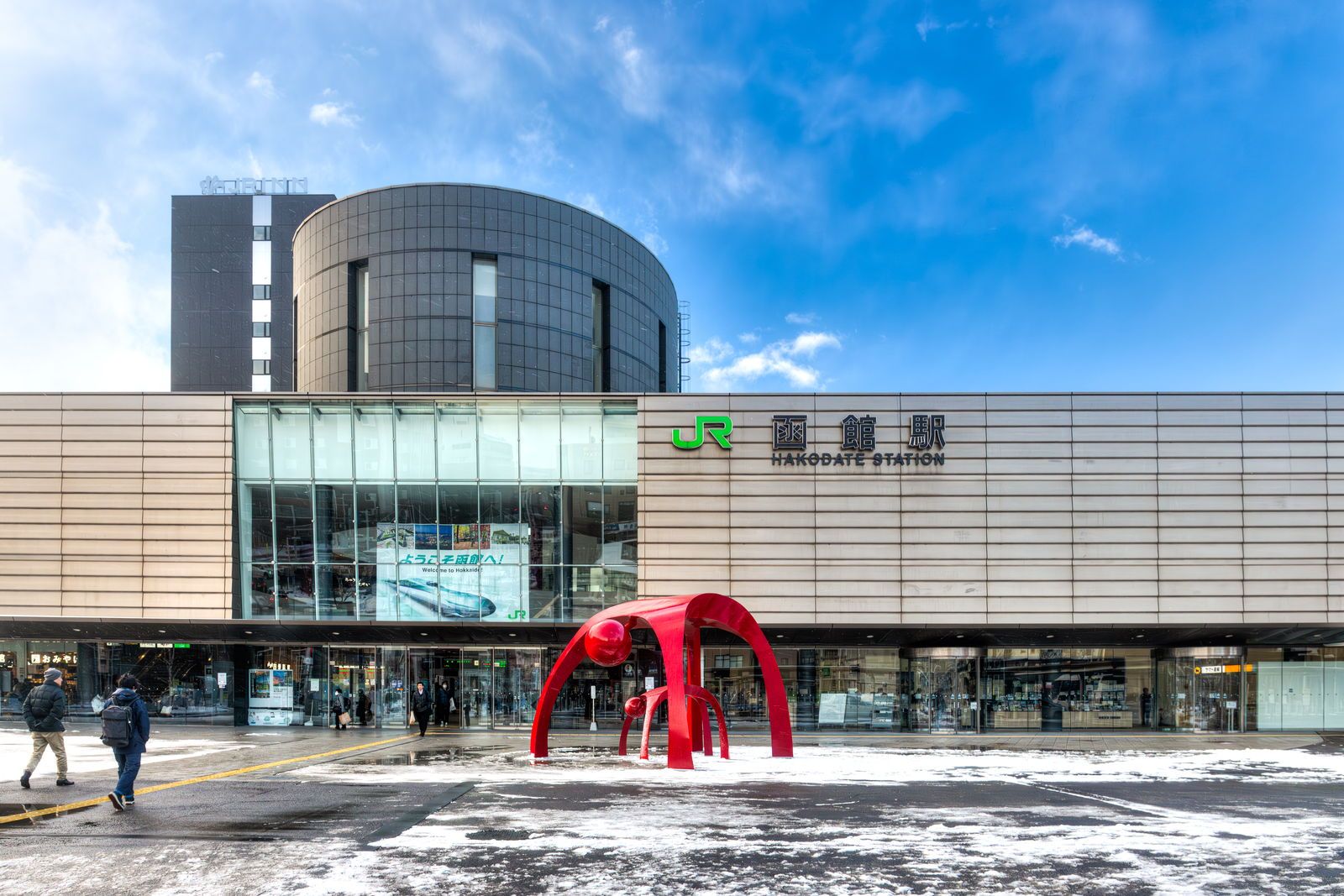 駅前広場に雪が残るJR函館駅の駅舎と赤いモニュメント