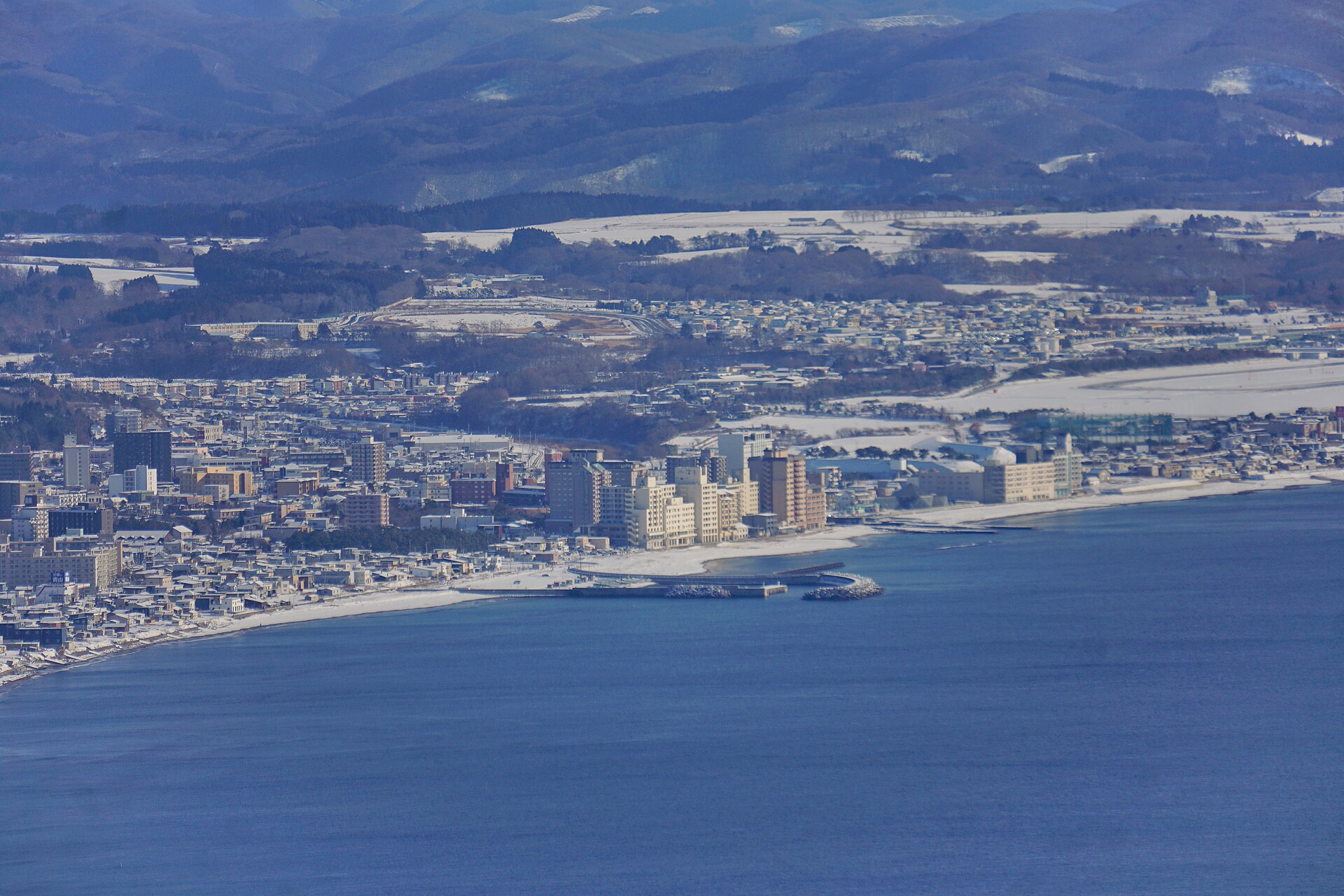 函館山から望む、海沿いに建物が並ぶ雪景色の湯の川温泉地区