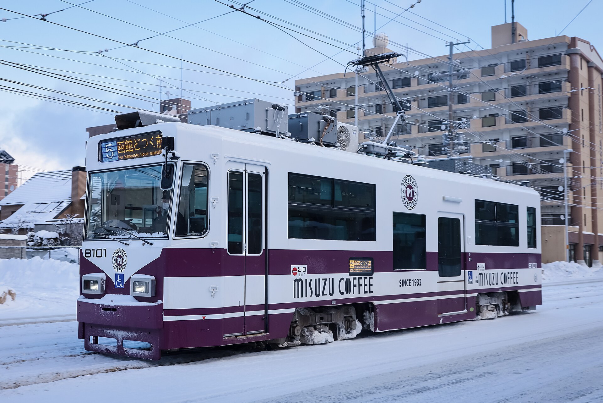 雪の積もった道路を走る白とえんじ色の函館市電の車両