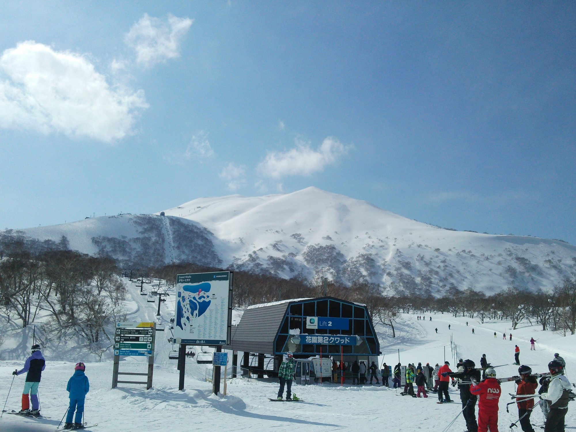 青空の下、雪をかぶったニセコアンヌプリを背にした花園第2クワッドの乗り場とスキーヤー