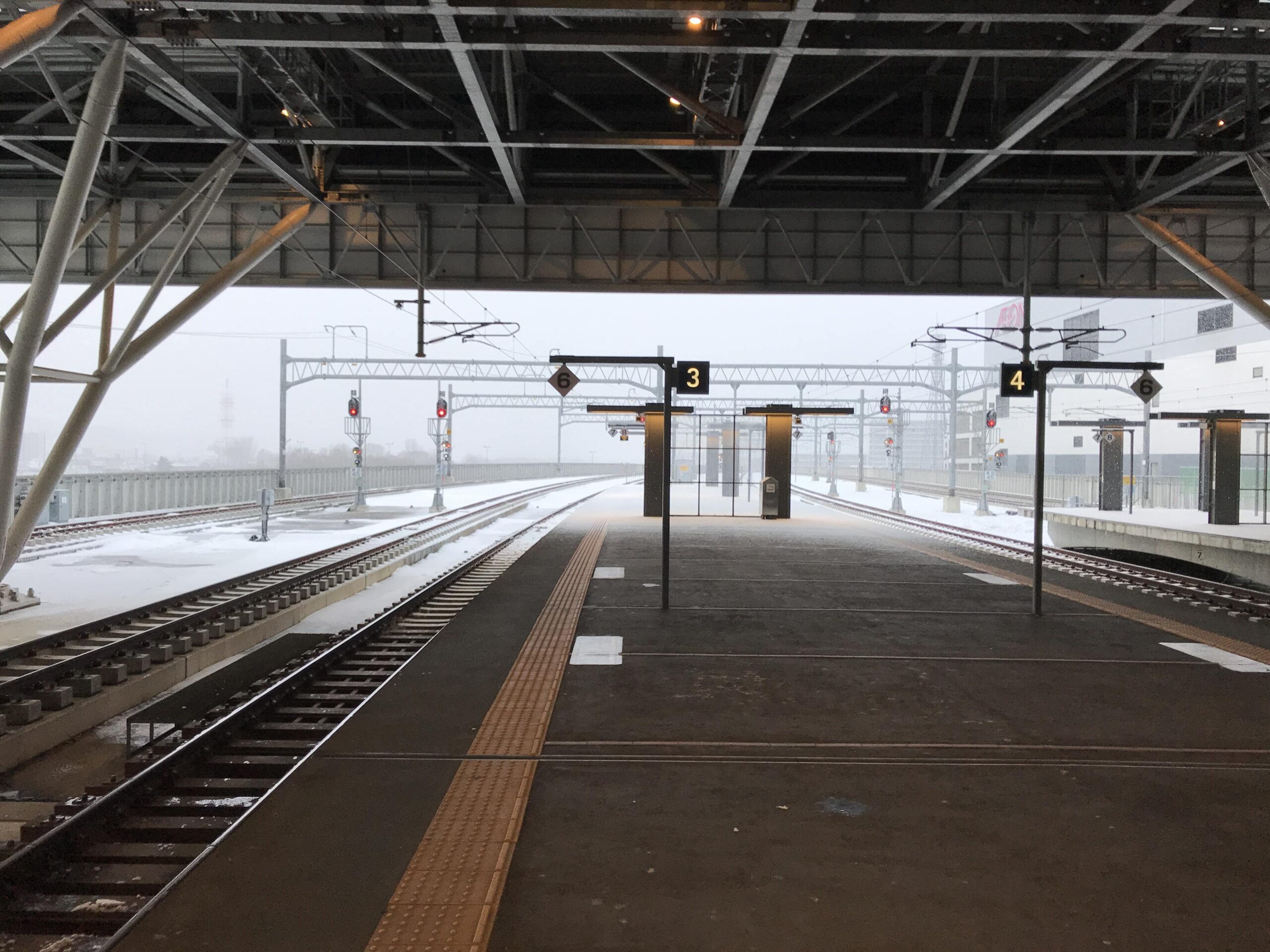 雪が降る日の旭川駅のホームと、線路脇に積もった雪