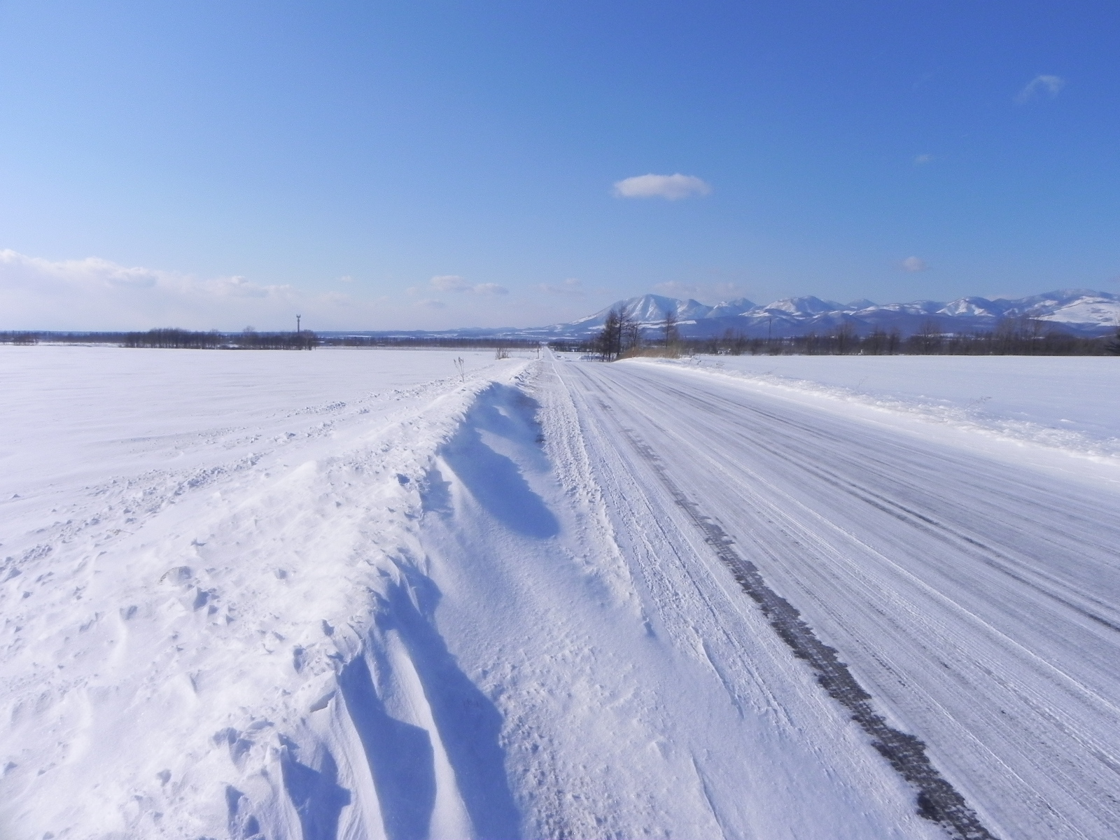 一面の雪原の中をまっすぐ延びる圧雪された道路と遠くの雪山