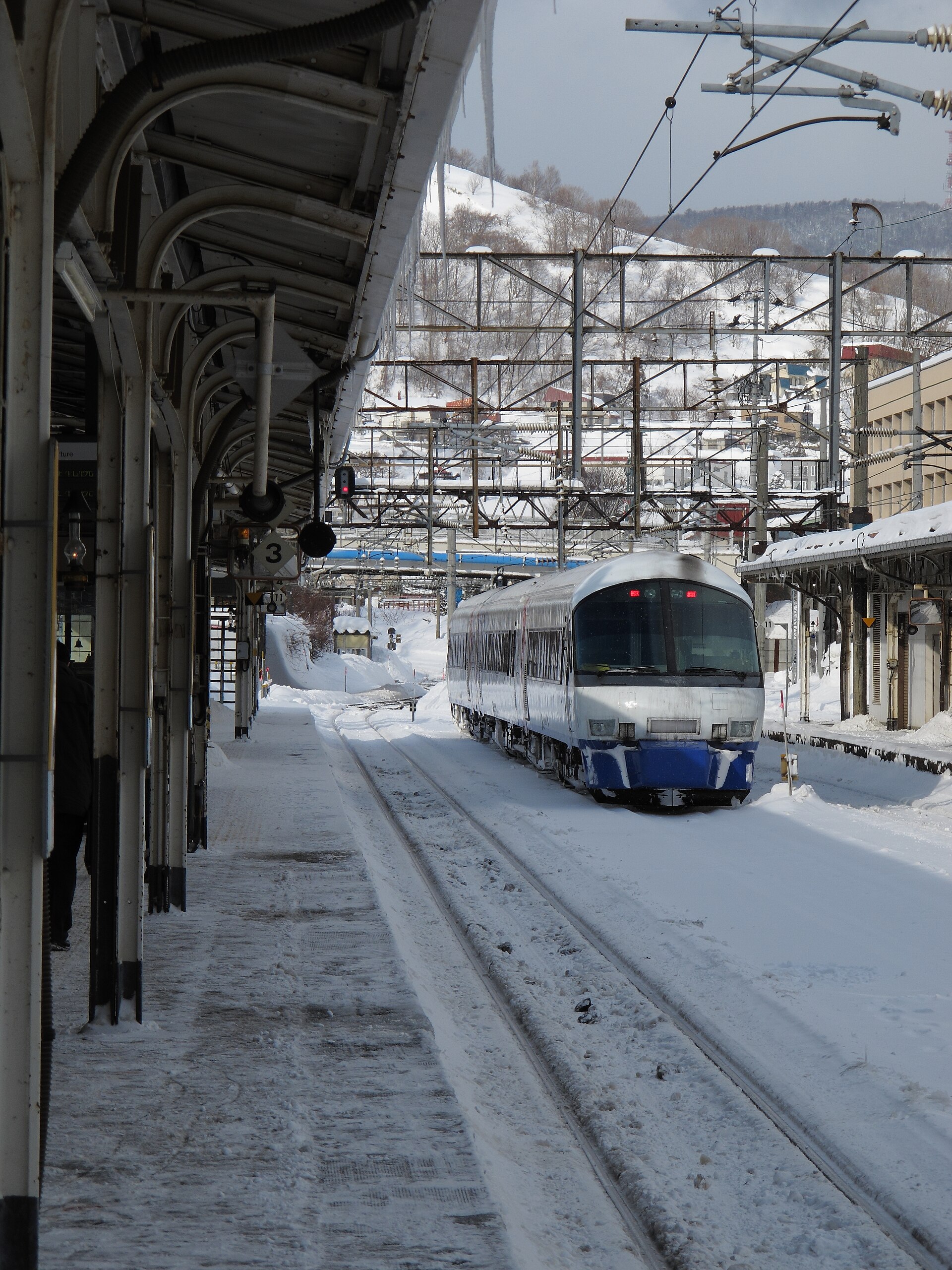 屋根に雪が積もった冬の小樽駅のホームと、雪の線路に停まる列車