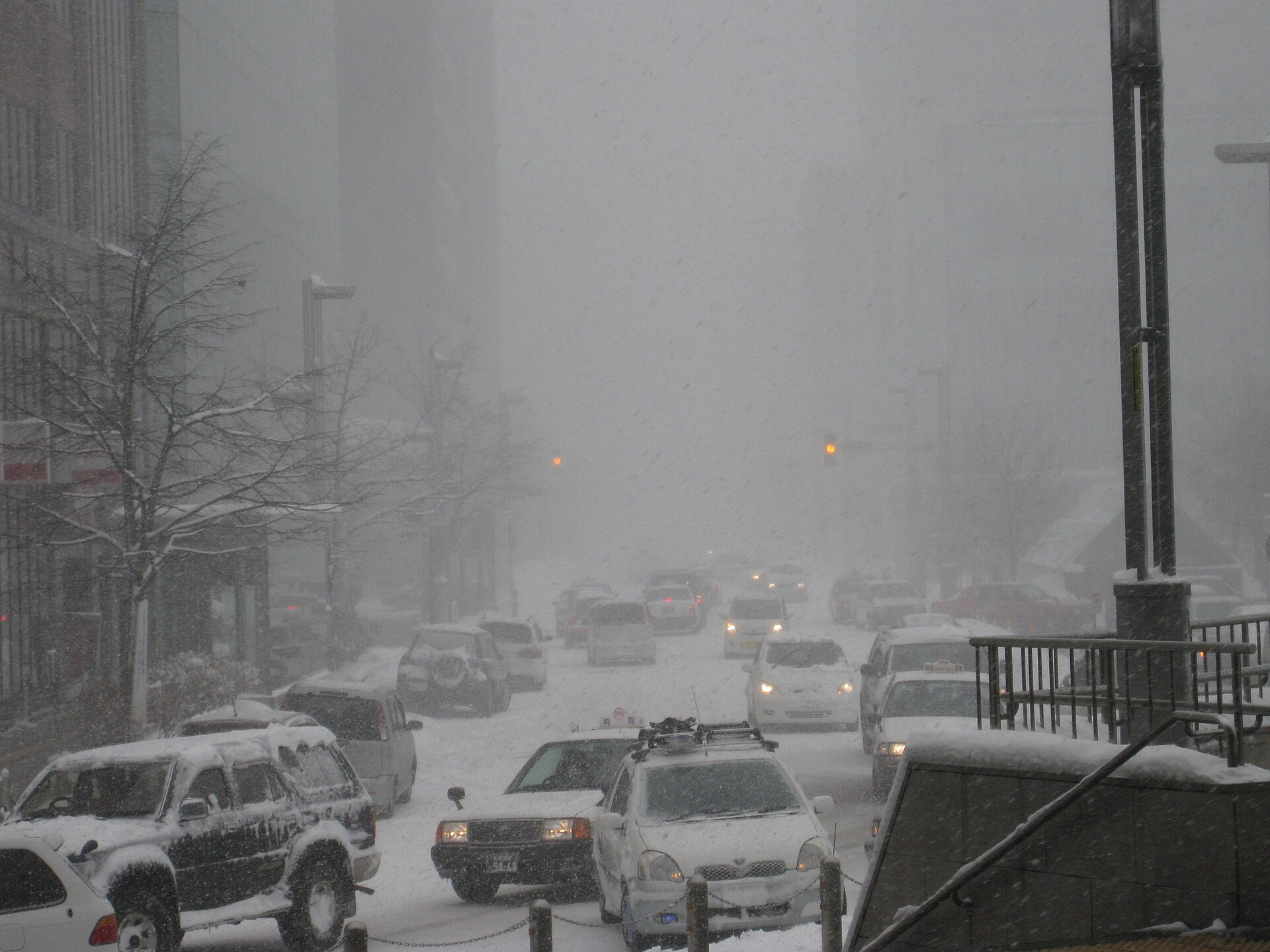 大雪で視界が白くかすむ札幌駅北側の道路と、雪をかぶった車の列