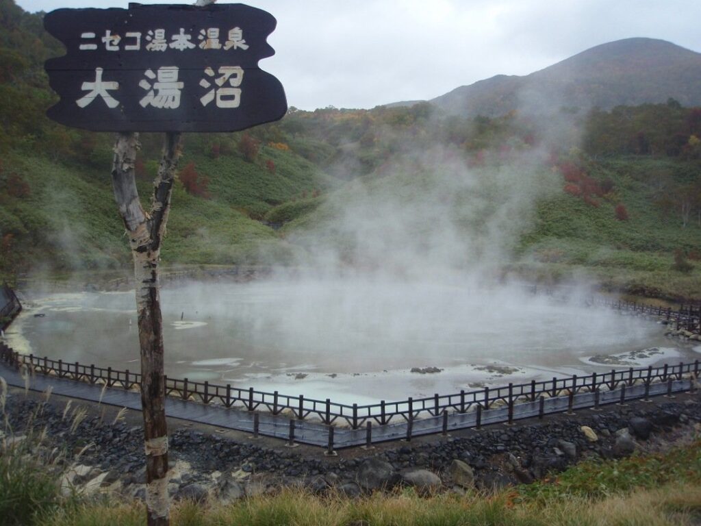 湯けむりが立ちのぼるニセコ湯本温泉の大湯沼と「大湯沼」の看板