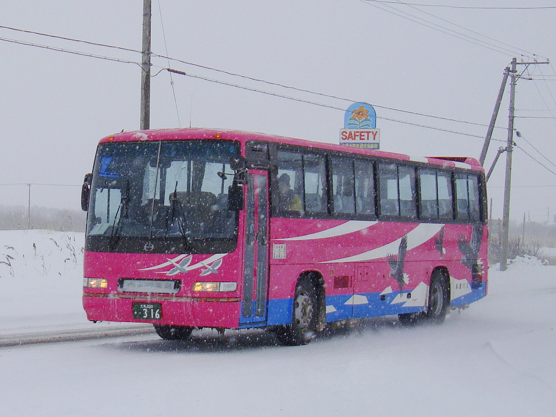 雪が降る中、雪道を走るピンク色の車体の大型バス