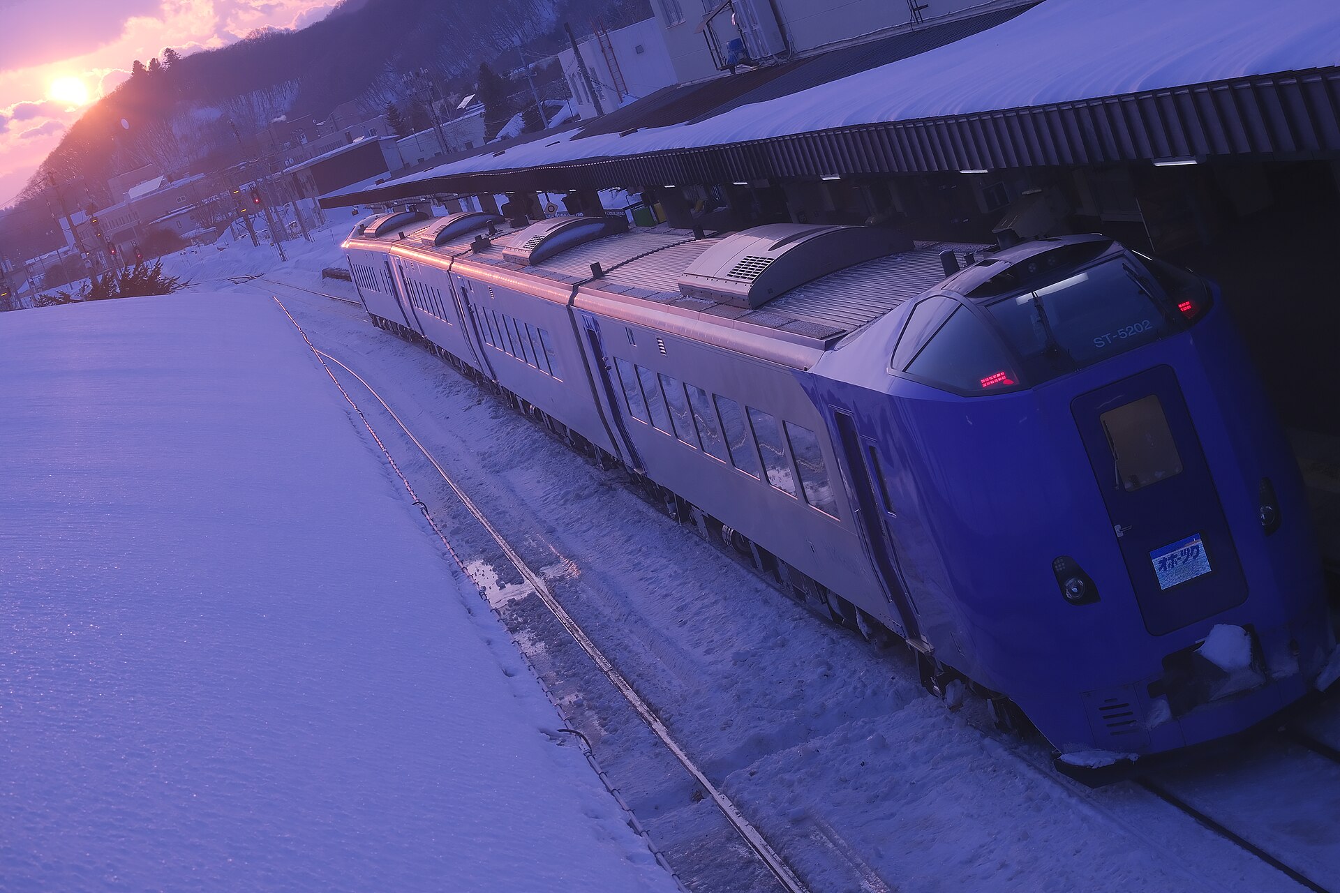 雪に覆われた駅のホームに停車している紫色の特急列車