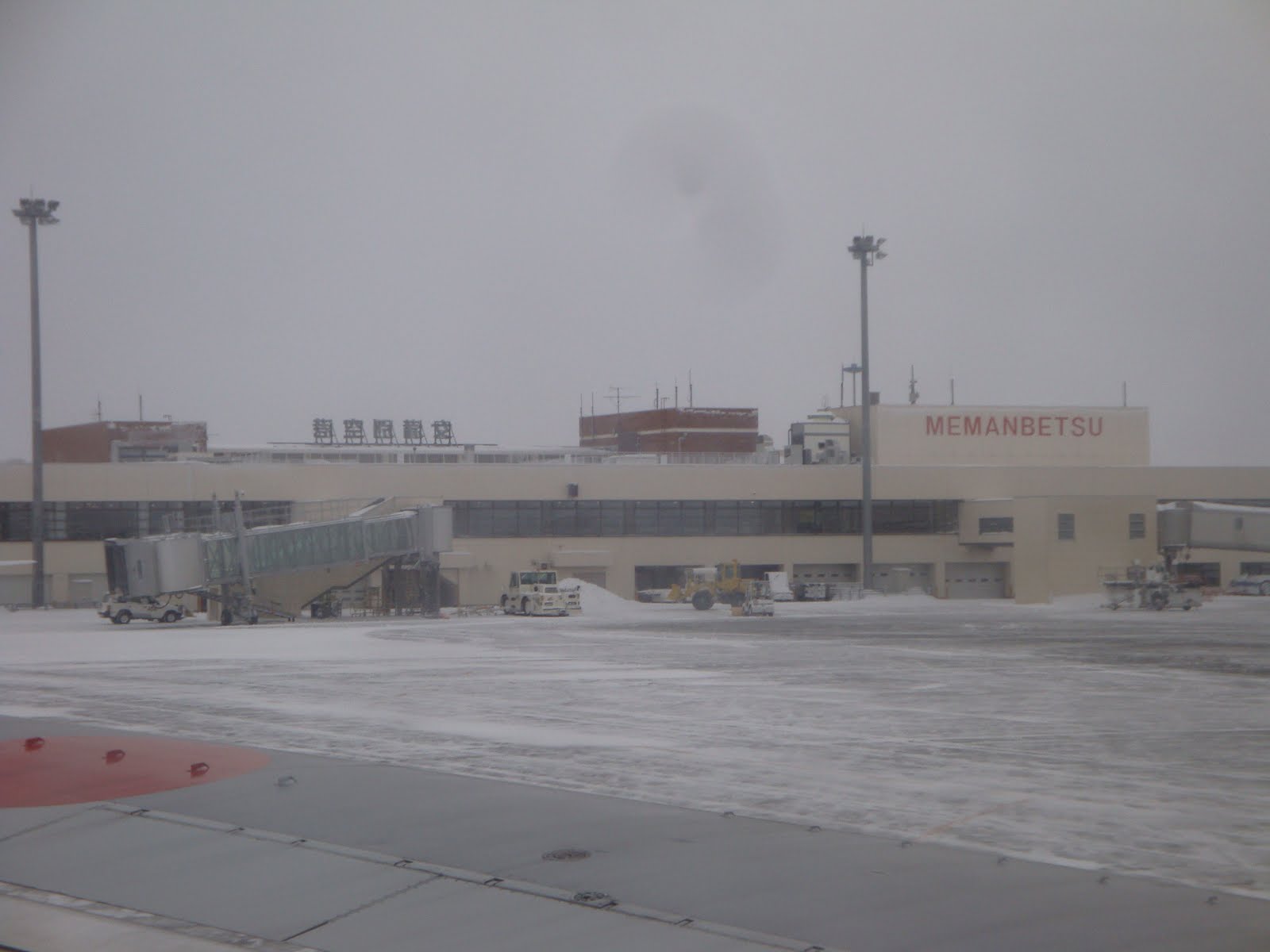 雪の降る日の空港。平屋のターミナルビルに「MEMANBETSU」の文字と搭乗橋が見える