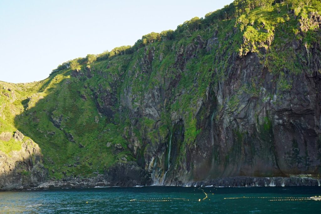 オホーツク海から見上げる知床半島の断崖と細く流れ落ちる「男の涙」の滝