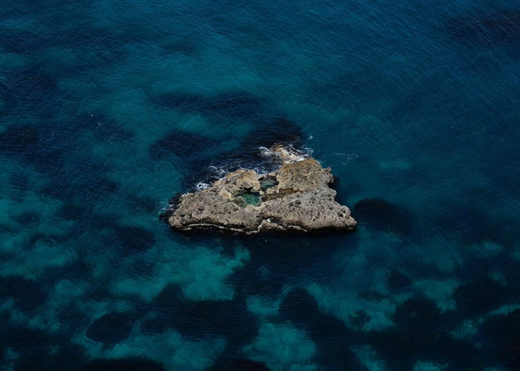積丹半島の先端沖に浮かぶ小島と、海底が透けて見える青い海の空撮