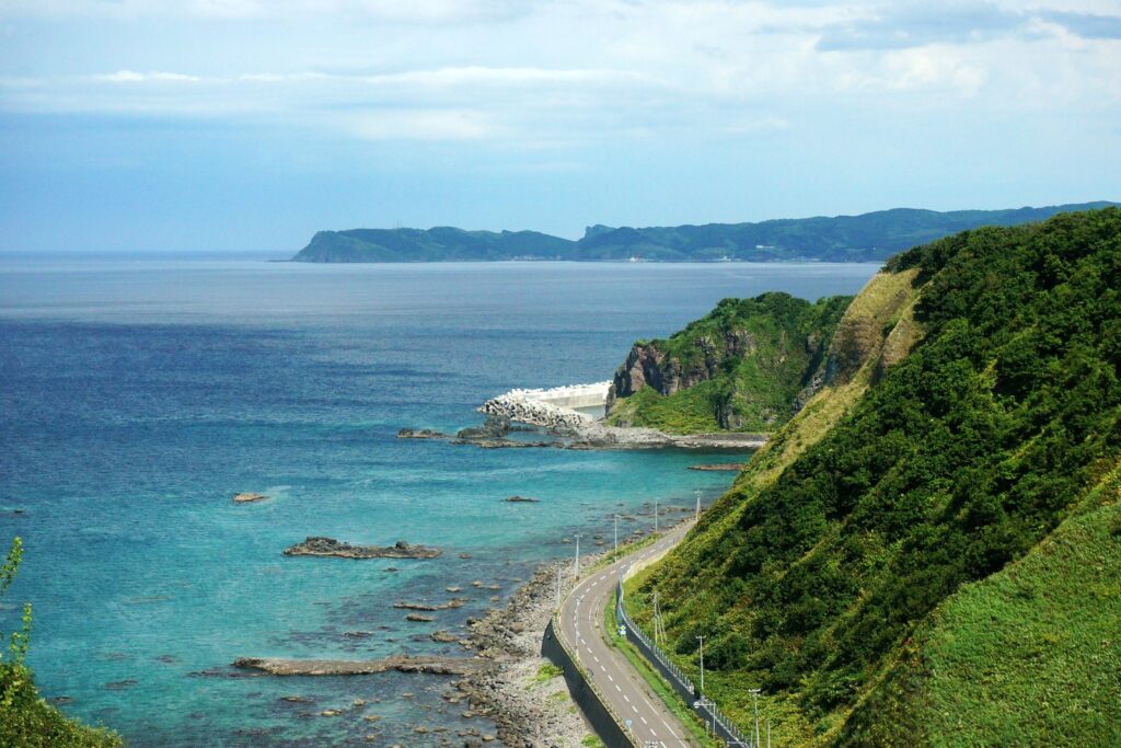 積丹岬から望む、緑の斜面の下を海沿いに延びる道路と青い海